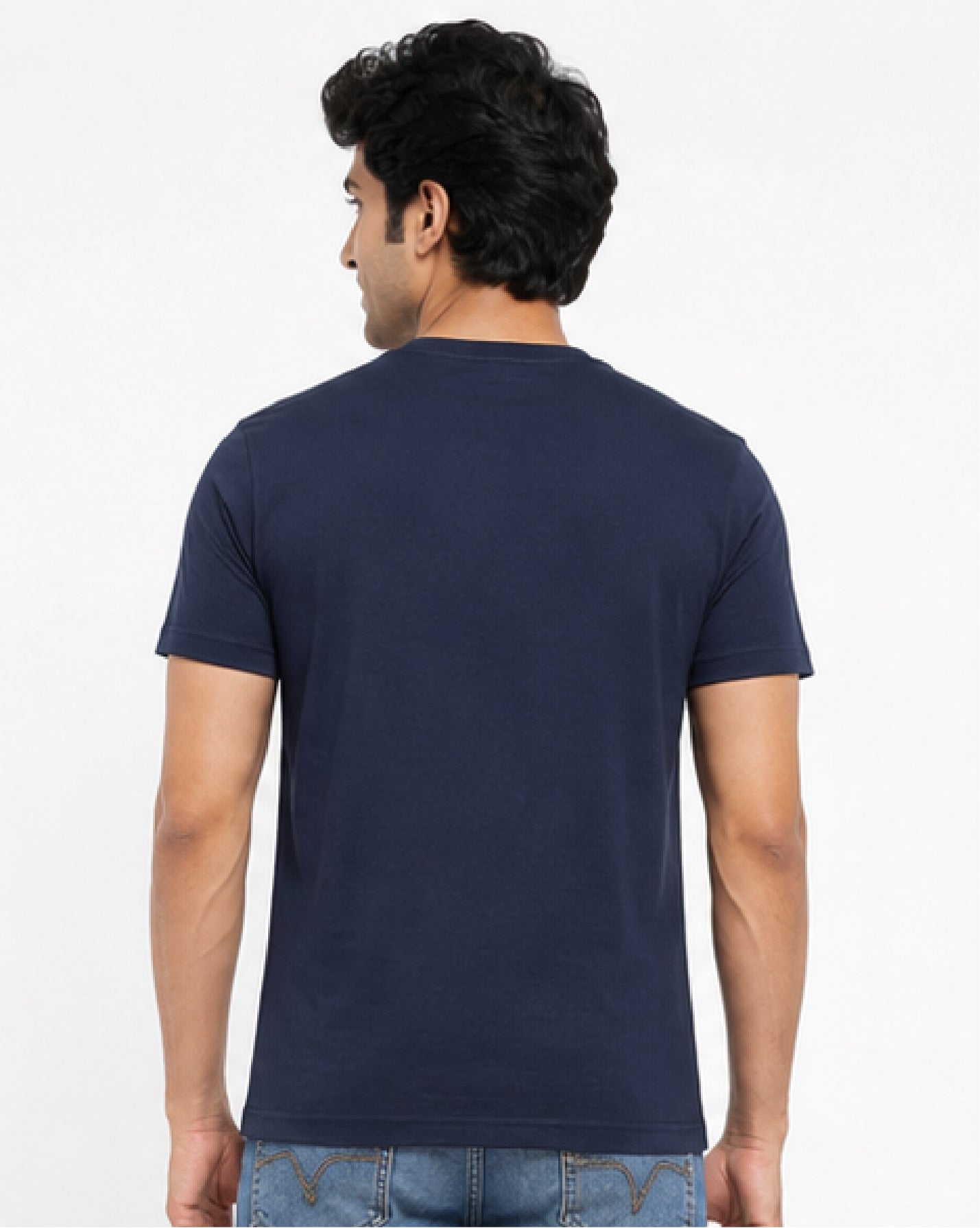 A man viewed from the back wearing a solid navy blue short-sleeve t-shirt and blue jeans, set against a plain white studio background.