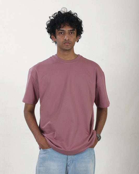 Man wearing a mauve t-shirt and light blue jeans against a white background