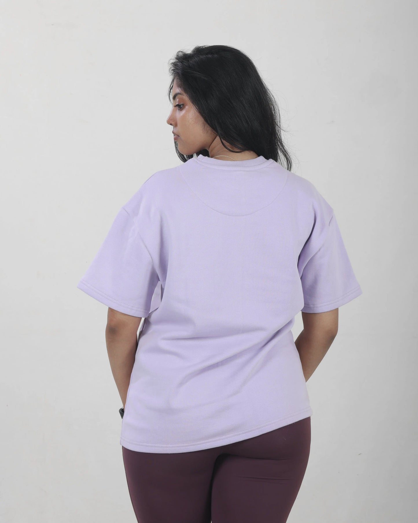 Person wearing a light purple t-shirt and maroon pants on a plain background