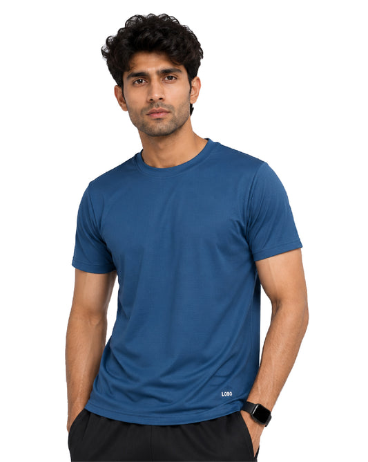 A man wearing a short-sleeve crew-neck athletic t-shirt in a medium blue color, paired with black shorts, against a plain white background.