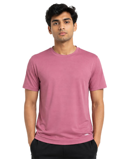 A man wearing a short-sleeve crew-neck athletic t-shirt in dusty rose pink, paired with black pants, photographed against a solid white background.