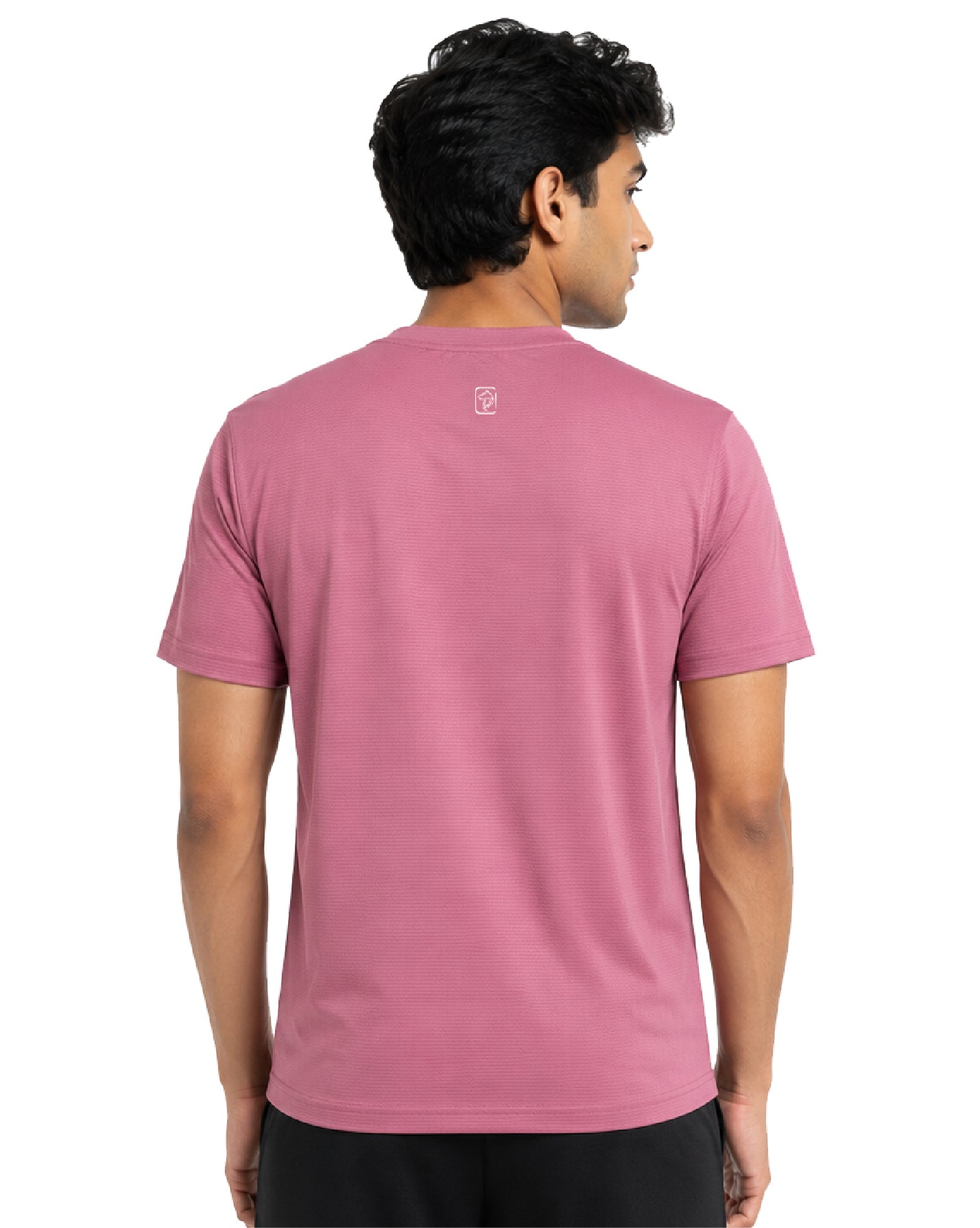 A man viewed from the back wearing a dusty rose pink short-sleeve crewneck t-shirt with a small white embroidered logo on the upper back, paired with black pants against a white background.