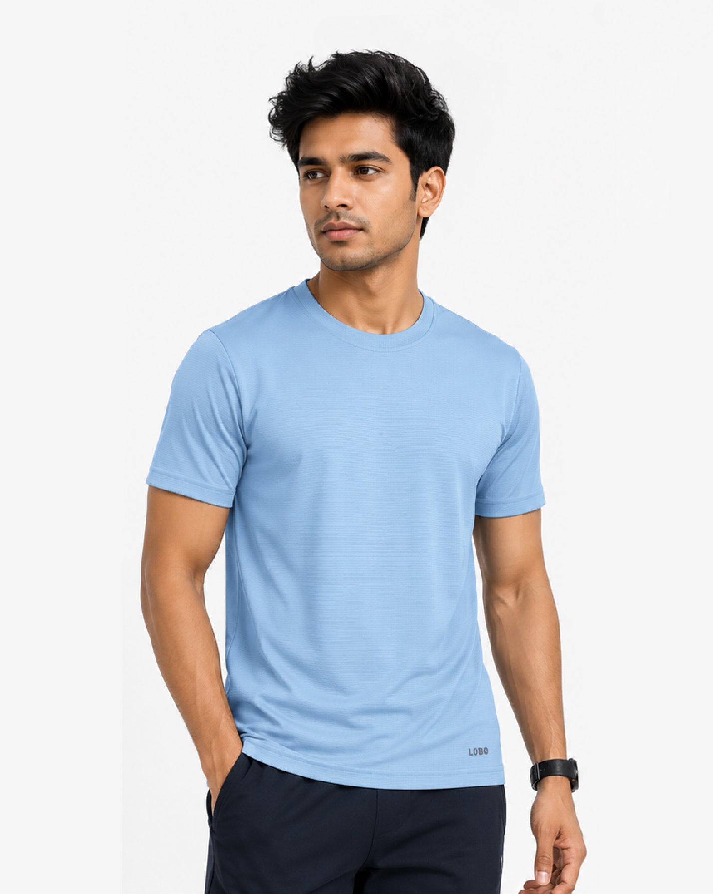 A man wearing a light blue crew-neck t-shirt and dark navy pants, standing against a plain light gray background.