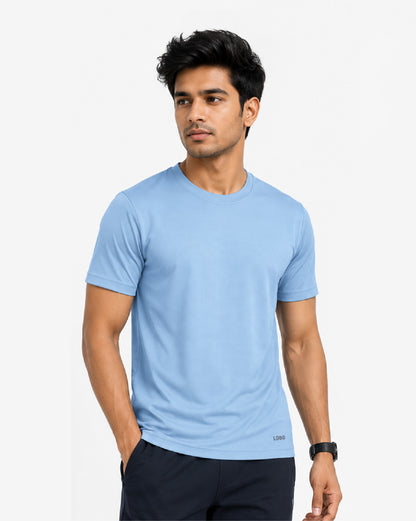 A man wearing a light blue crew-neck t-shirt and dark navy pants, standing against a plain light gray background.